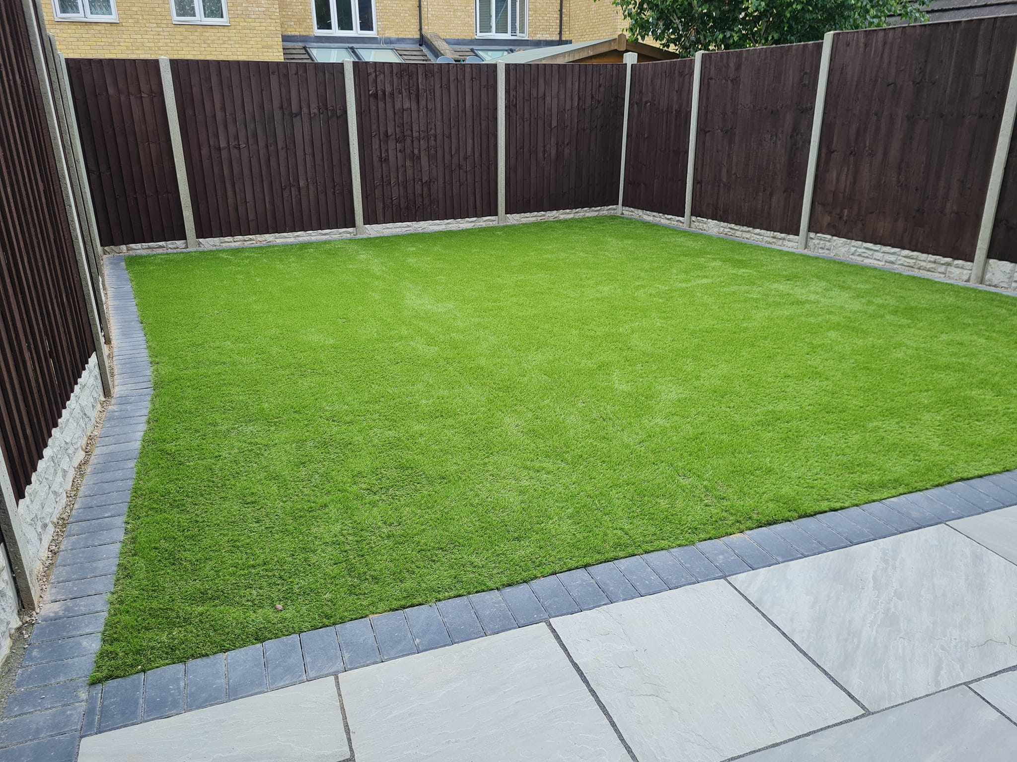 Artificial grass with paving border and panel fencing